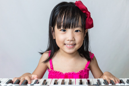 Asian Chinese little girl playing electric piano keyboard in isolated white background.の写真素材