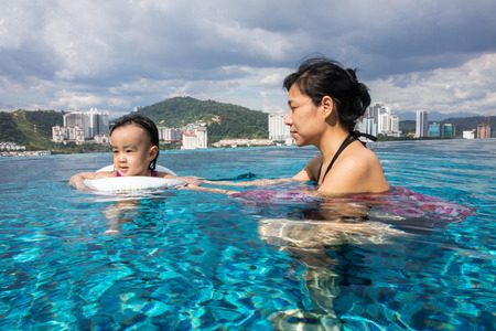 Asian Chinese mother and daugther playing at outdoor swimming pool on sunny dayの写真素材