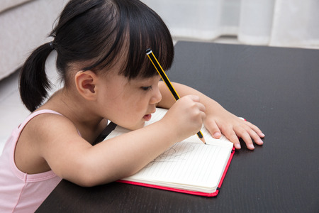 Asian Chinese little girl writing on exercise book in the living room at home.の写真素材