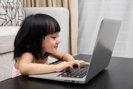 Smiling Asian Chinese little girl using laptop in the living room at homeの写真素材