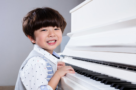 Happy Asian Chinese little boy playing piano in the living room at home.の写真素材