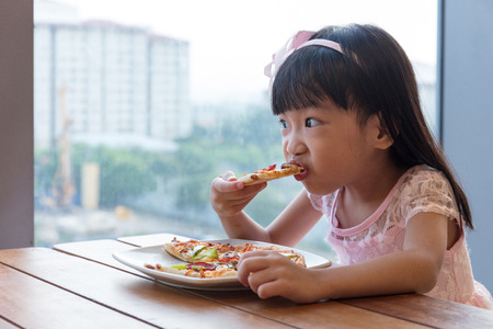 Asian Chinese little girl eating pizza pepperoni in the restaurant.の写真素材