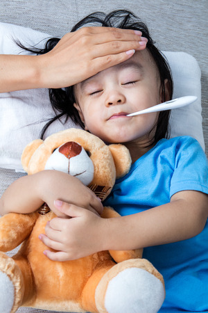 Asian Chinese mother measuring little girl forehead for fever at home.の写真素材