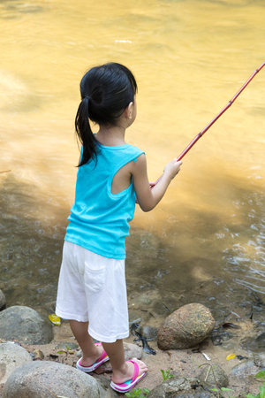 Asian Chinese little girl angling with fishing rod at the river shore.の写真素材
