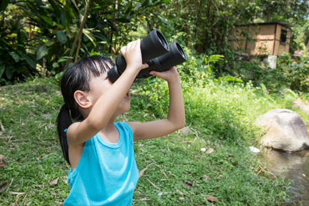 Asian Chinese little girl exploring around with binoculars in the forestの写真素材