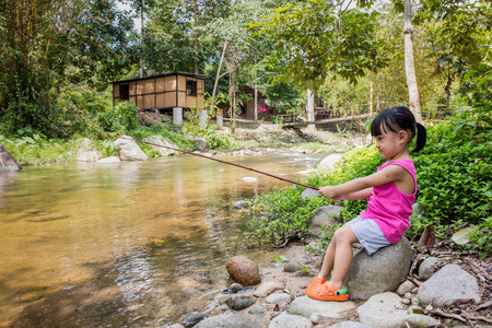 Happy Asian Chinese little girl angling with fishing rod at the river shore.の写真素材