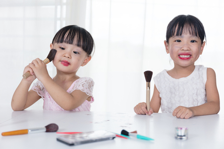 Asian Chinese little sisters having fun with cosmetics makeup in the dressing room at home.の写真素材