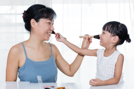 Asian Chinese mother and daughter having fun with cosmetics makeup in the dressing room at home.の写真素材