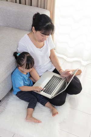 Happy Asian Chinese mother and daughter using laptop on the floor at home.の写真素材