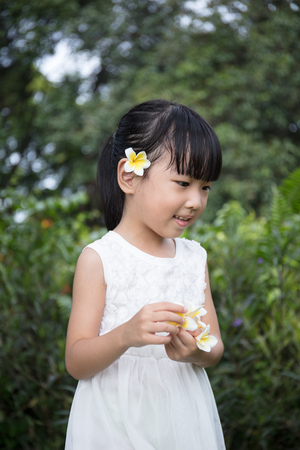 Asian Chinese little girl holding flowers in outdoor garden on day timeの写真素材