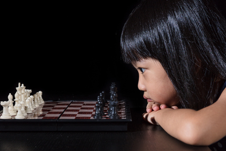 Asian Little Chinese girl playing chess in isolated black backgroundの写真素材