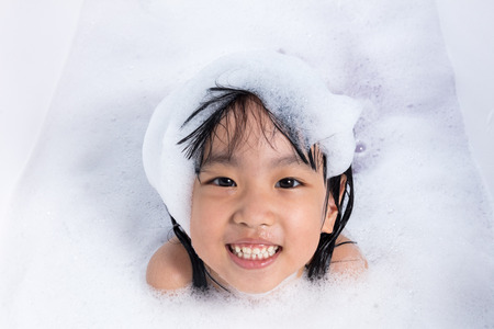 Asian little Chinese girl playing with water and foam in bathtub at homeの写真素材