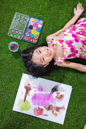 Asian Chinese little girl lying on the grass drawing and paintingの写真素材