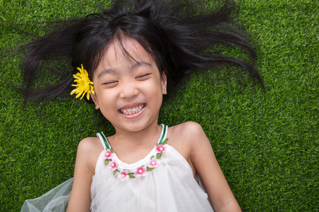 Asian Chinese little girl lying on the grass with flower at outdoor parkの写真素材