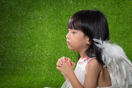 Asian Chinese little girl wearing angel wings and praying at outdoor parkの写真素材