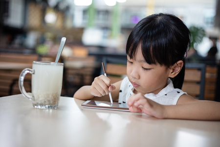 Asian Chinese little girl playing smartphone at outdoor cafeの写真素材