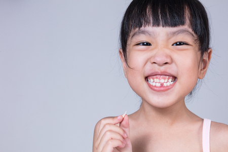 Asian Chinese little girl holding her missing tooth in isolated white backgroundの写真素材