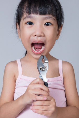 Asian Chinese little girl holding pliers and showing the gap in isolated white backgroundの写真素材