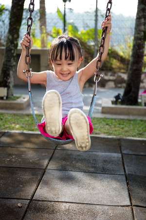 Asian little Chinese girl playing swing at outdoor parkの写真素材