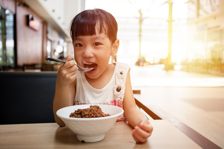Asian little Chinese girl eating braised pork rice in outdoor cafeの写真素材