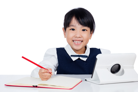 Asian Chinese little girl in uniform studying with tablet computer in isolated white backgroundの写真素材