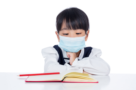 Asian Little Chinese girl reading book with protection mask in isolated white backgroundの写真素材
