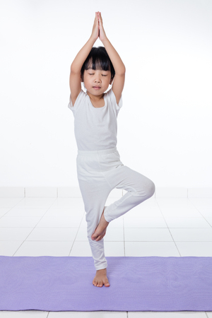 Asian Chinese little girl practicing yoga pose on a mat indoorの写真素材