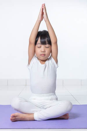 Asian Chinese little girl practicing yoga pose on a mat indoorの写真素材