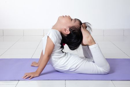 Asian Chinese little girl practicing yoga pose on a mat indoorの写真素材