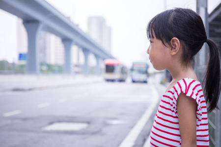 Asian Chinese little girl waiting for a bus at bus stopの写真素材