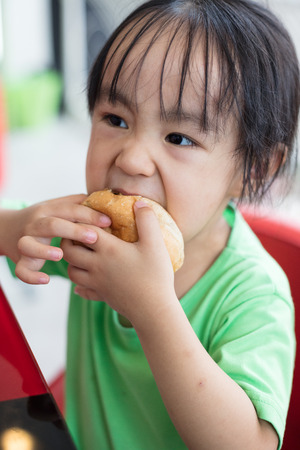 Asian little Chinese girl eating bread in outdoor cafeの写真素材