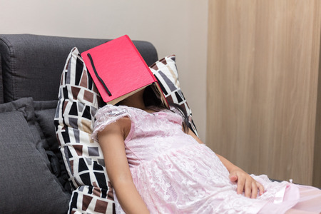 Asian Chinese little girl lying on the sofa with book in the living roomの写真素材