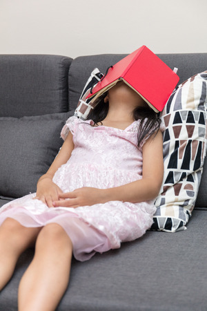 Asian Chinese little girl lying on the sofa with book in the living roomの写真素材