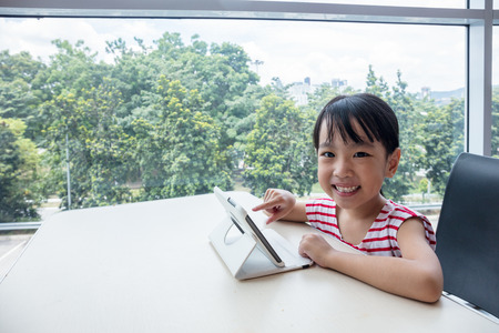 Asian Chinese little girl playing tablet computer at homeの写真素材
