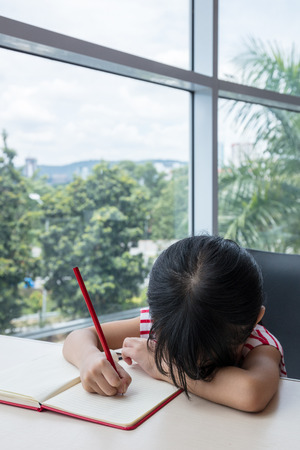 Boring asian little Chinese girl writing homework at homeの写真素材