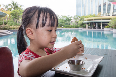 Asian Little Chinese Girl Eating Fried chicken at Outdoor Cafeの写真素材