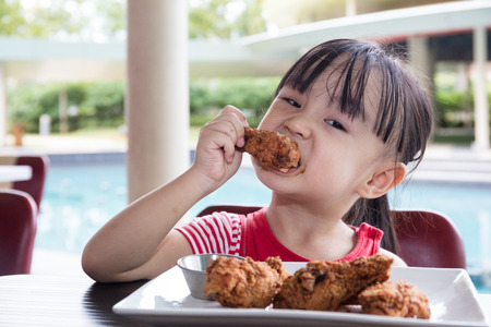 Asian Little Chinese Girl Eating Fried chicken at Outdoor Cafeの写真素材