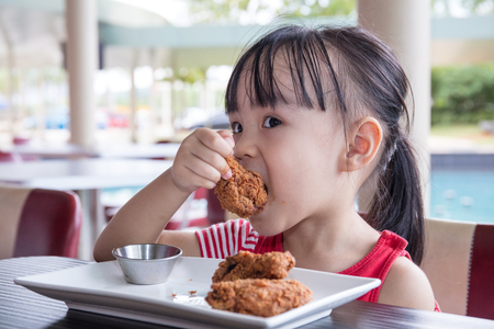 Asian Little Chinese Girl Eating Fried chicken at Outdoor Cafeの写真素材