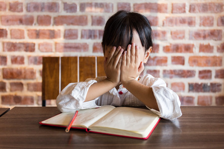 Frustrated Asian chinese little girl doing homework at homeの写真素材