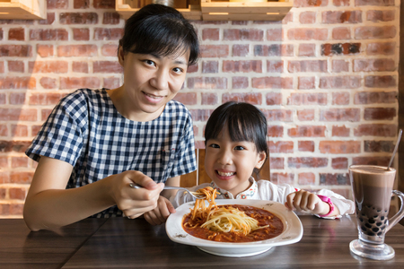 Asian Chinese mother and daughter eating spaghetti bolognese in the restaurantの写真素材