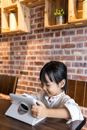 Asian Chinese little girl playing tablet computer at indoor cafeの写真素材