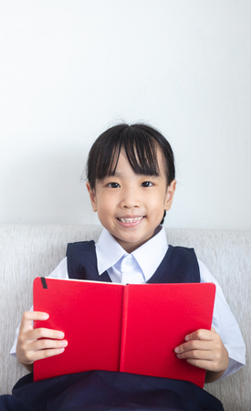 Asian Chinese little girl sitting on the sofa reading book in the living room at homeの写真素材