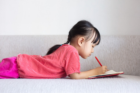 Asian Chinese little girl laying on the sofa writing book in the living roomの写真素材