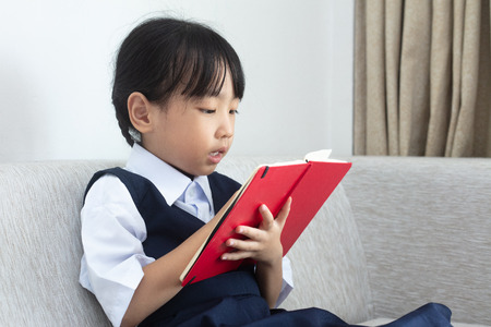 Asian Chinese little girl sitting on the sofa reading book in the living room at home
