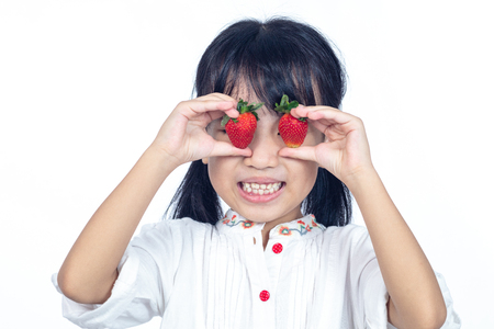Happy Asian Chinese little girl using strawberry as glasses in isolated white backgroundの写真素材