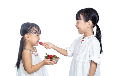 Asian Little Chinese sisters Eating Strawberry in isolated white backgroundの写真素材