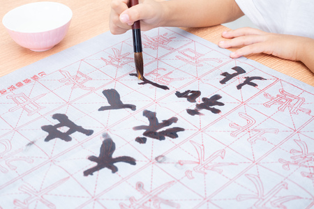 Close up of children hands holding brush to practice Chinese calligraphy at home