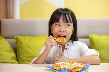 Asian Little Chinese Girl Eating pizza at restaurantの写真素材