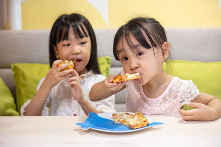 Asian Little Chinese sisters Eating pizza at restaurantの写真素材