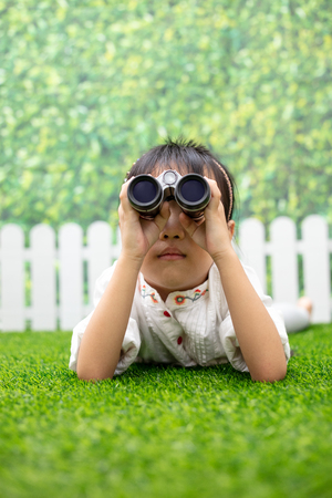 Asian Little Chinese girl kneeling on the grass and playing with telescope at outdoor parkの写真素材